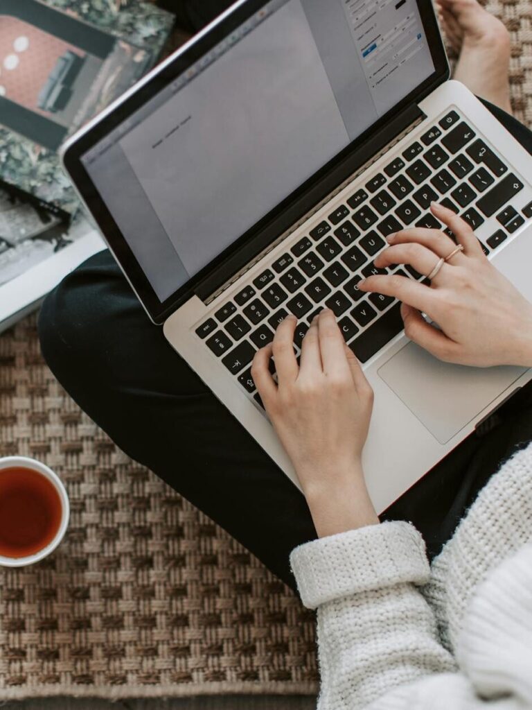 crop young businesswoman using laptop while drinking tea at home